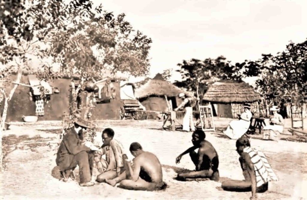 Misión de la  Iglesia Profética de Victoria Falls. Foto donde se ve que mientras el misionero adoctrina, sus mujeres leen o cosen y un carpintero trabaja.